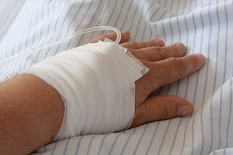 Close-up of elderly hand with IV drip and bandage on hospital bed