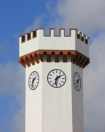 White Clock Tower with Brown Crenellations Against Blue Sky