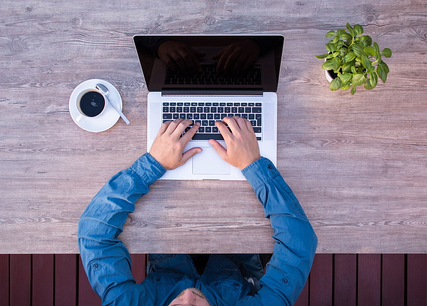 Top View of Man Typing on Laptop with Coffee and Plant