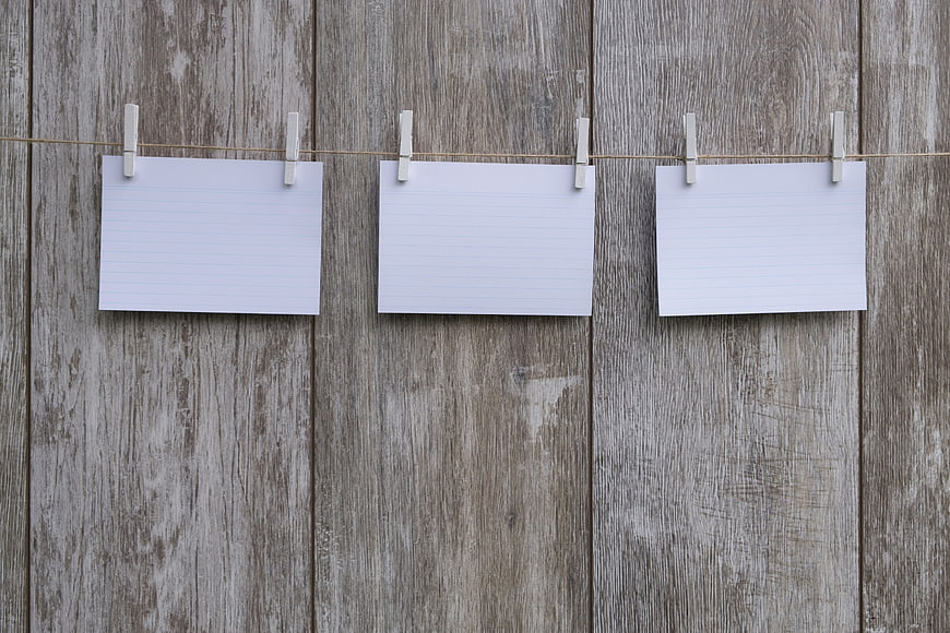 Blank lined paper sheets hanging on clothesline against rustic wood