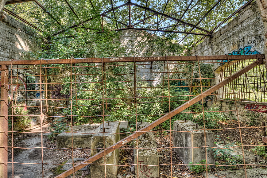 Abandoned concrete bunker with rusty metal fence and overgrown vegetation