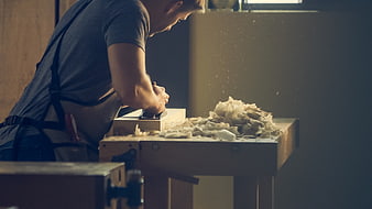 Carpenter planing wood with hand plane in workshop