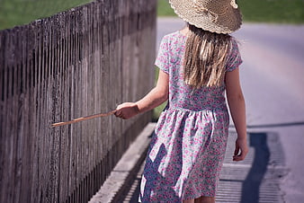 Little Girl in Floral Dress Walking Along Wooden Fence