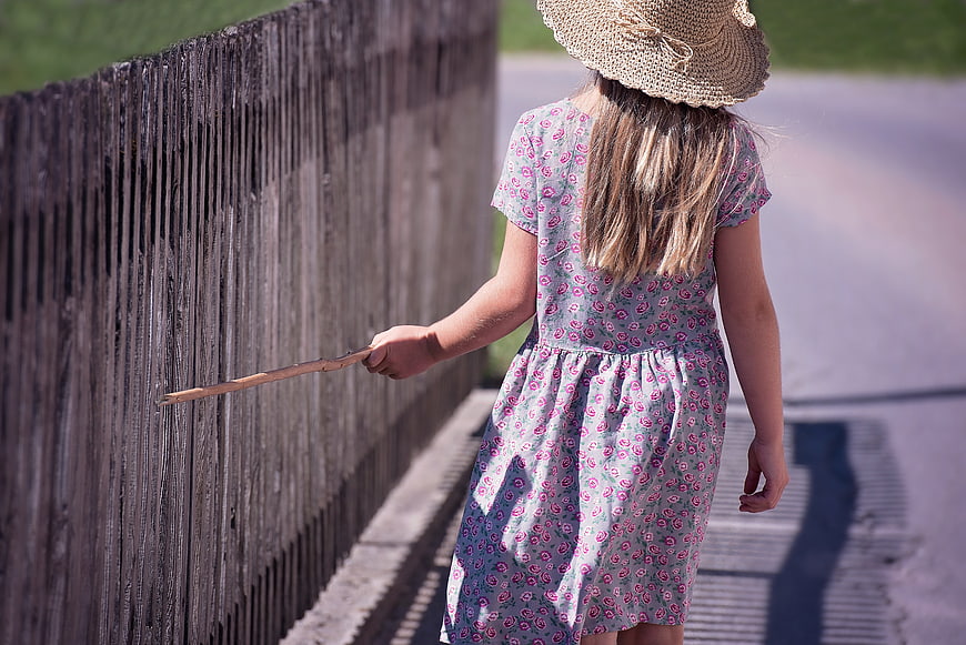 Little Girl in Floral Dress Walking Along Wooden Fence