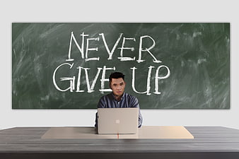 Man working on laptop in front of chalkboard with never give up text
