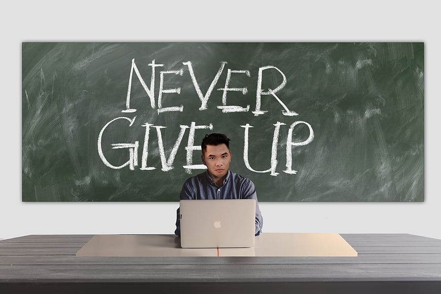 Man working on laptop in front of chalkboard with never give up text