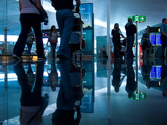 Travelers with luggage reflected in airport terminal floor