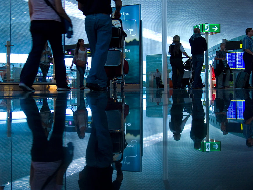 Travelers with luggage reflected in airport terminal floor
