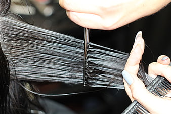Close-up of hairdresser cutting dark hair with scissors