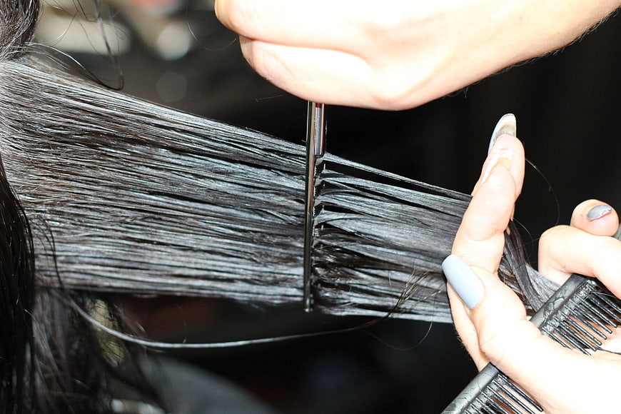Close-up of hairdresser cutting dark hair with scissors