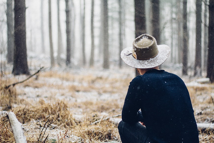 Man in Fedora Sitting Alone in Snowy Winter Forest