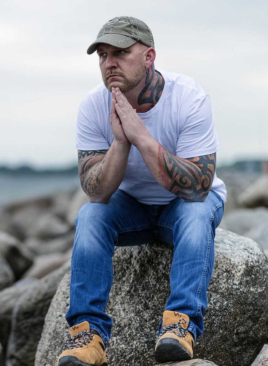 Pensive tattooed man sitting on rocks by the sea
