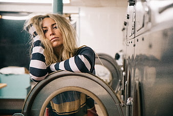 Tired blonde woman leaning on washing machine in laundromat