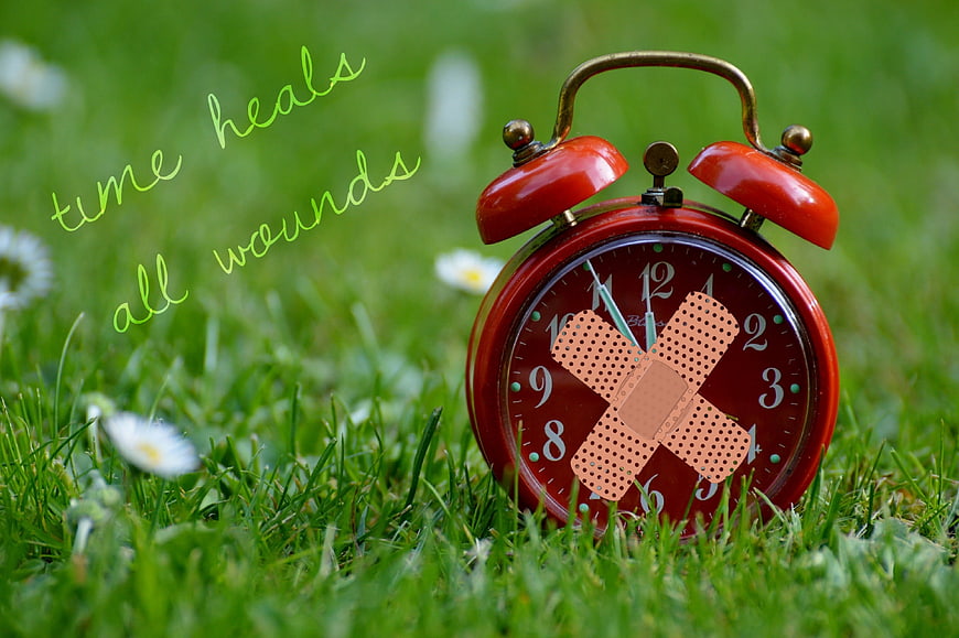 Red alarm clock with bandage on grass symbolizing healing