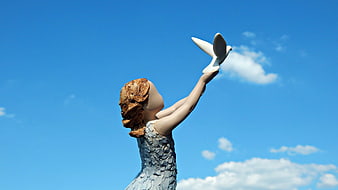 Statue of woman releasing white dove against blue sky
