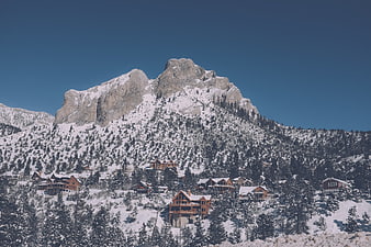 Snowy Mountain Peak with Ski Resort Cabins and Pine Trees