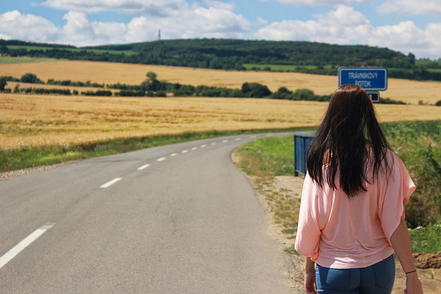 Woman Hitchhiking on Rural Road with Blue Sign
