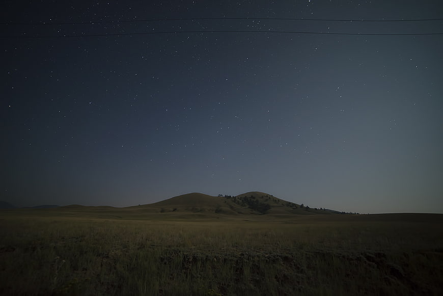 Starry Night Sky Over Rolling Hills and Grassy Field