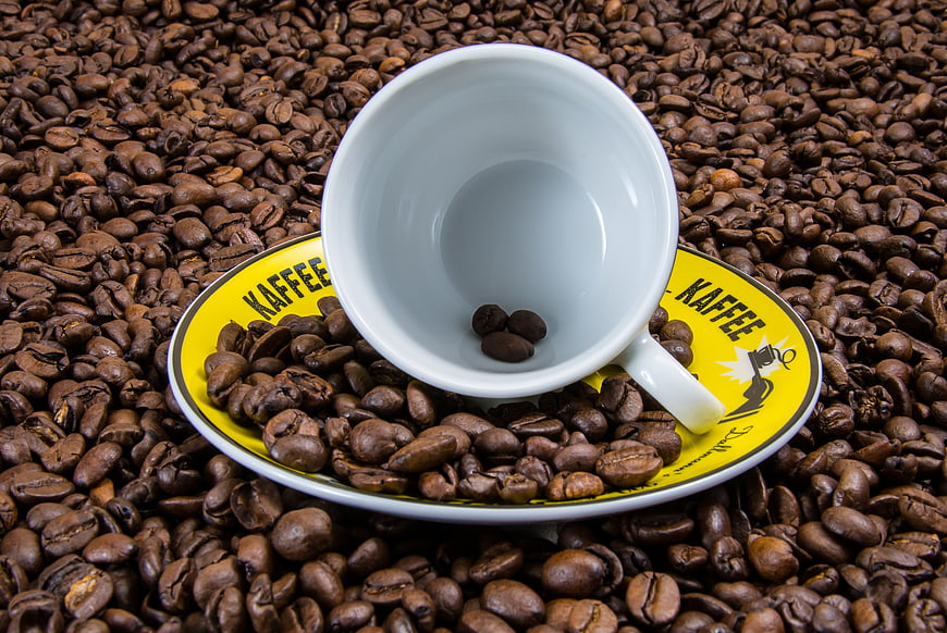 White Coffee Cup On Saucer Surrounded By Roasted Coffee Beans