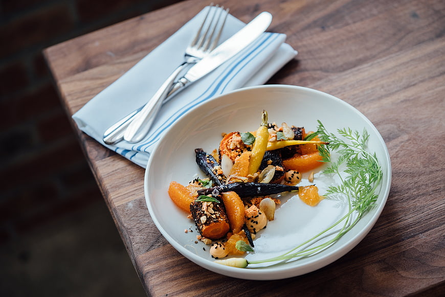 Gourmet roasted carrots on white plate with cutlery