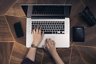 Top view of hands typing on laptop with camera lens and wallet