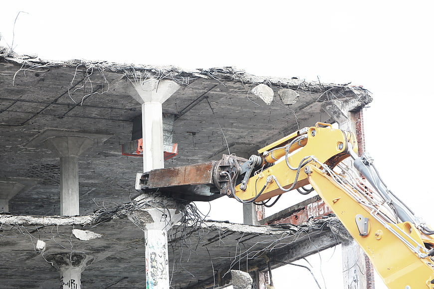 Yellow Excavator Demolishing Concrete Building Structure