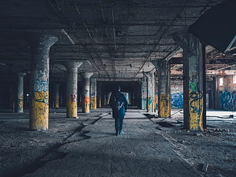 Man with Backpack Walking Through Abandoned Industrial Warehouse