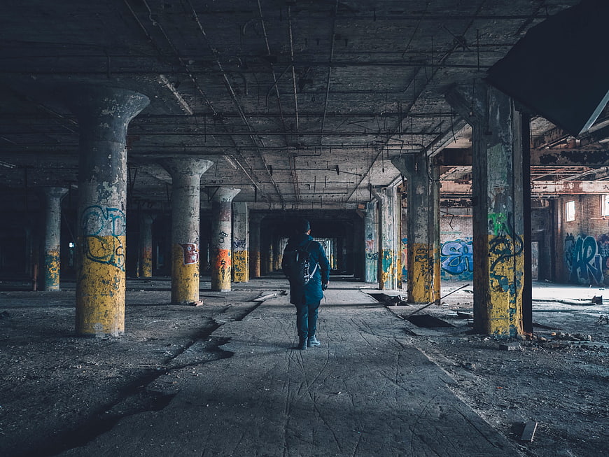 Man with Backpack Walking Through Abandoned Industrial Warehouse