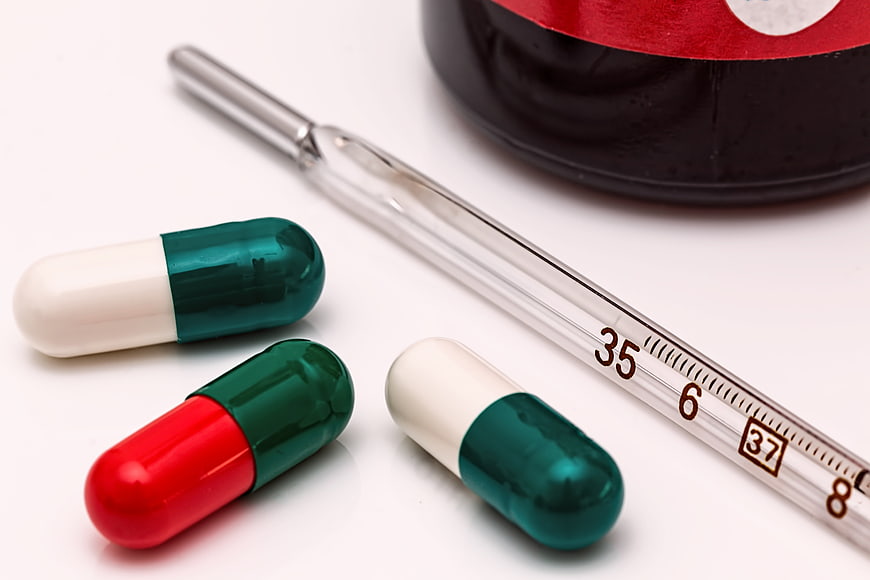 Medical thermometer and colorful capsules on white background