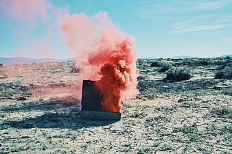Orange smoke grenade erupting from vintage suitcase in desert