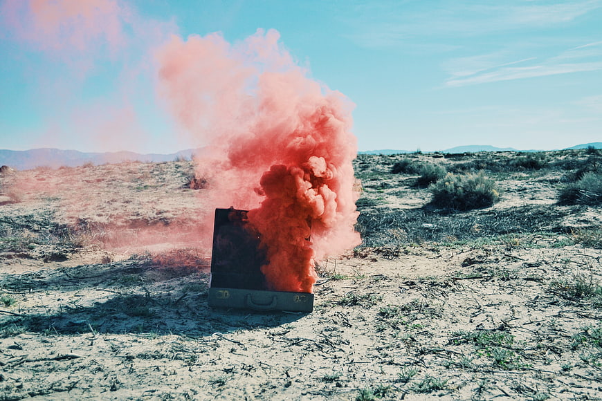 Orange smoke grenade erupting from vintage suitcase in desert