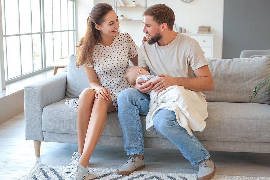 Young Parents Holding Newborn Baby on Sofa