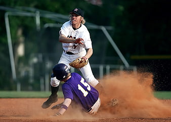 Baseball players sliding into base with dust cloud