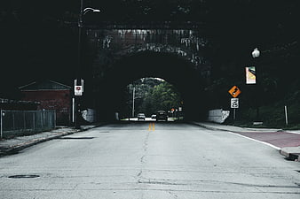 Road leading under dark stone arch bridge tunnel