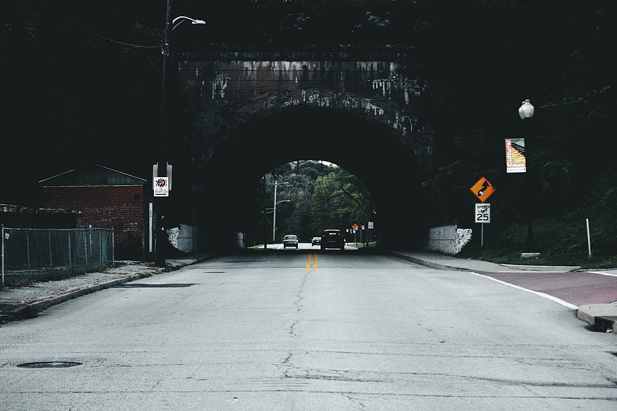 Road leading under dark stone arch bridge tunnel