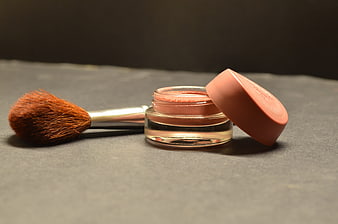 Open cosmetic jar with makeup brush on dark textured surface