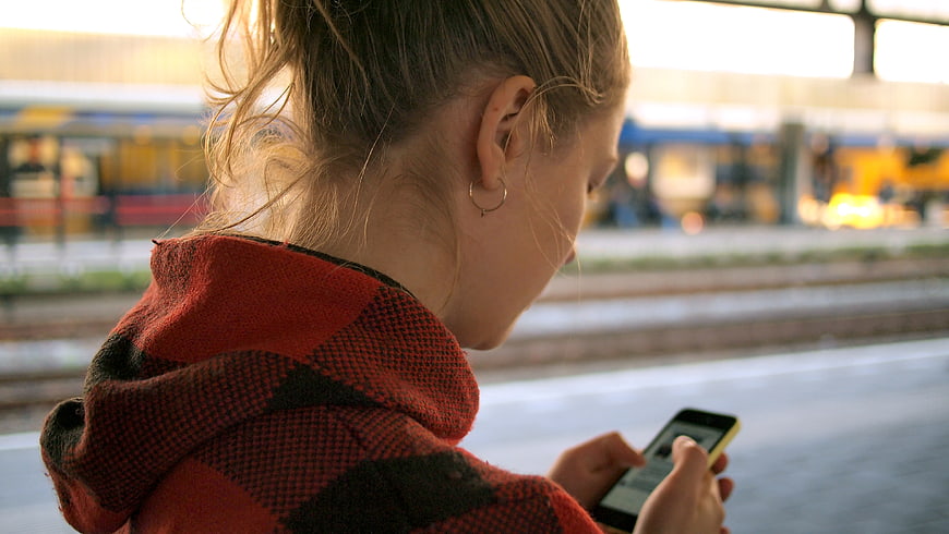 Woman in Red Plaid Hoodie Using Smartphone at Train Station