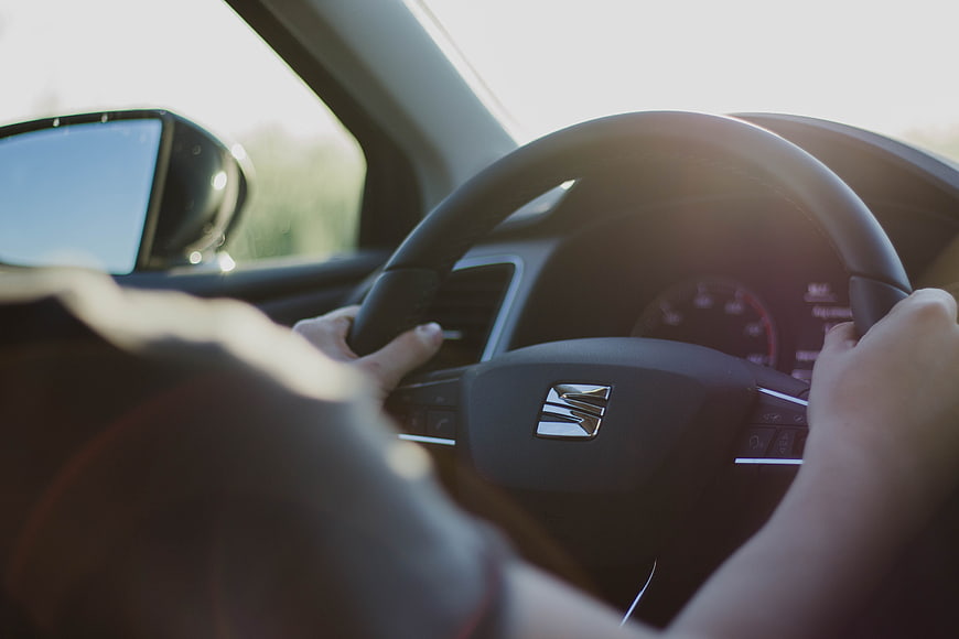Hands on car steering wheel driving in sunlight