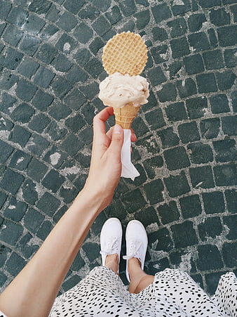 First-person view of woman holding ice cream cone on cobblestone street