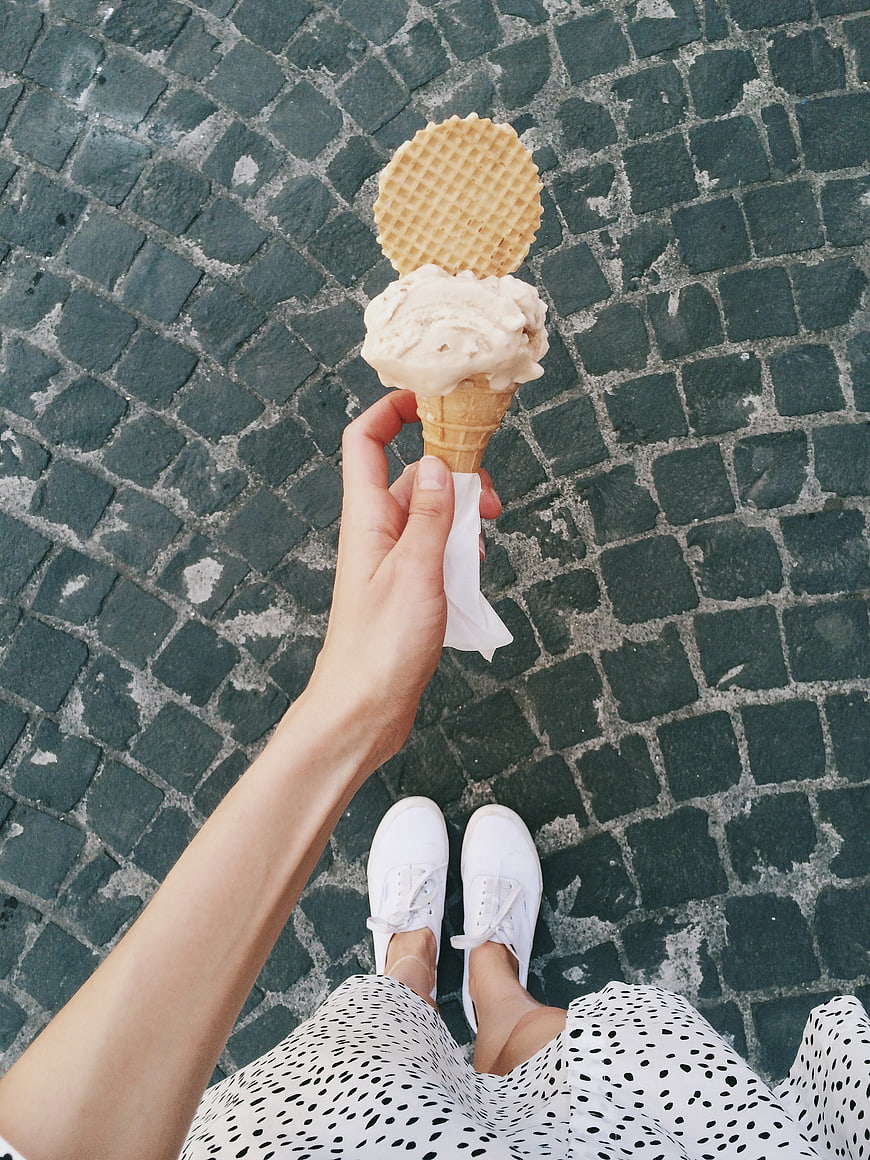 First-person view of woman holding ice cream cone on cobblestone street
