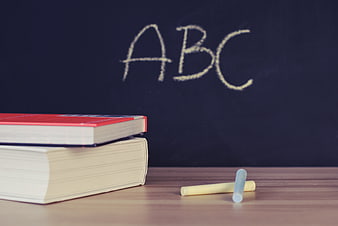 ABC written on chalkboard with books and chalk on desk