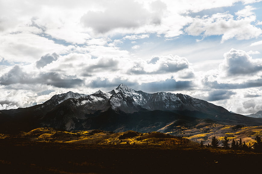 Dramatic Mountain Landscape with Golden Autumn Forest and Cloudy Sky