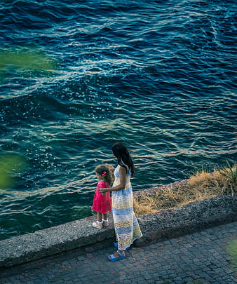 Mother and daughter looking at ocean waves from stone wall