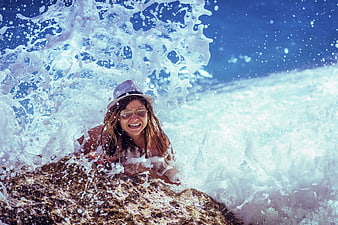 Happy woman laughing in ocean wave splash on rocks