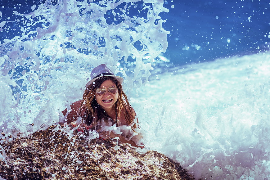 Happy woman laughing in ocean wave splash on rocks