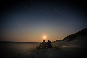 Couple watching moonrise over starry beach dunes