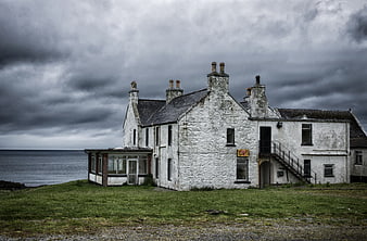 Abandoned white stone building on a grassy cliff overlooking the sea under a stormy sky