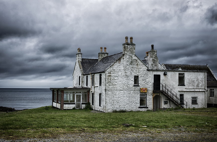 Abandoned white stone building on a grassy cliff overlooking the sea under a stormy sky