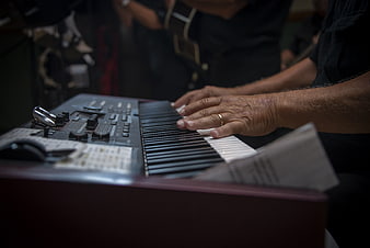Close-up of senior hands playing a digital keyboard in a dimly lit music studio