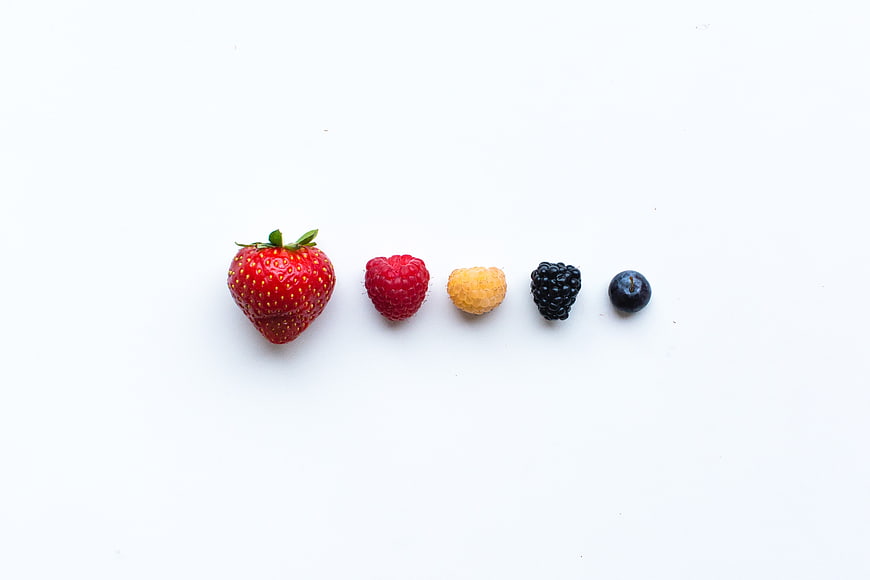 Fresh mixed berries arranged in a row on white background